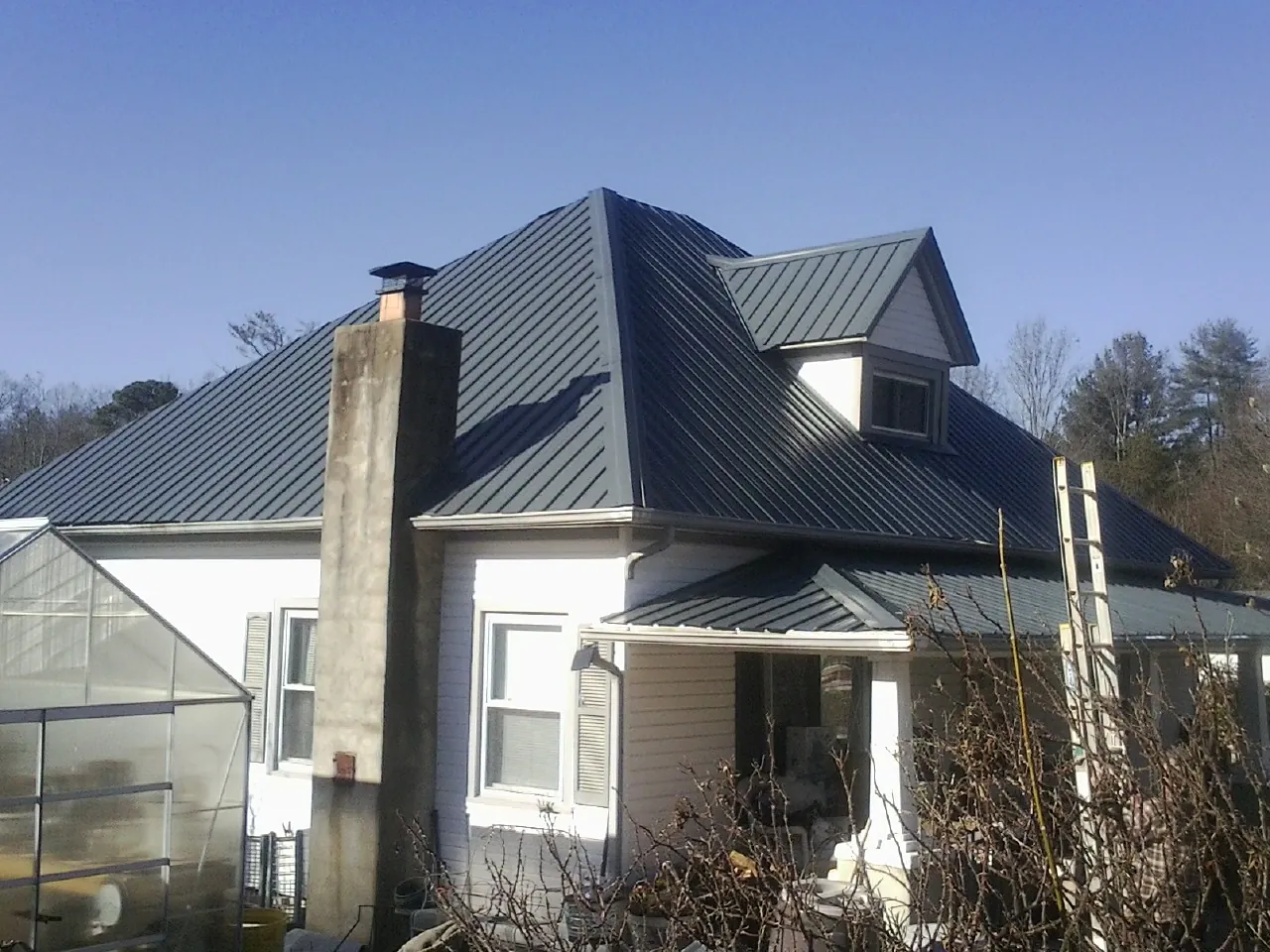 Dark blue standing seam metal roof on a white farmhouse with dormer — Slate & Tile Roof Repair by Roofing Brothers in Council Bluffs