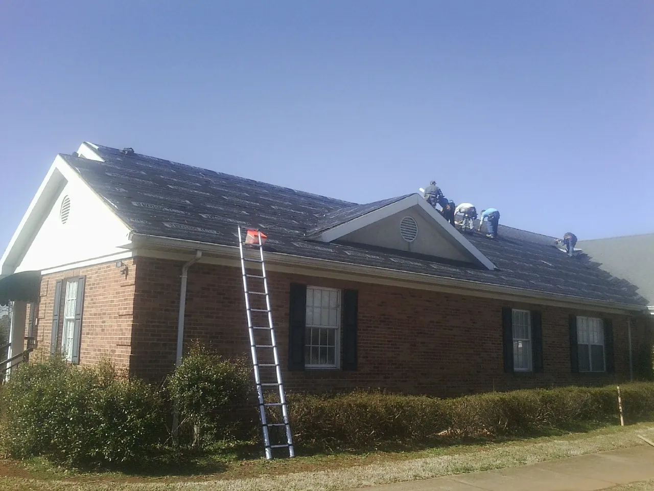 Crew tearing shingles off a brick ranch roof with a ladder set — Metal Roof Repair work by our crew in Council Bluffs