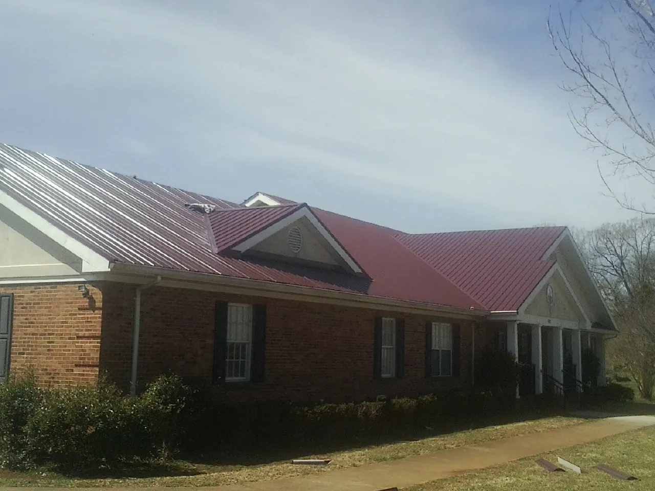 Red metal roof with gabled entries on a long brick building, from a Hail Damage Roof Repair job in Council Bluffs