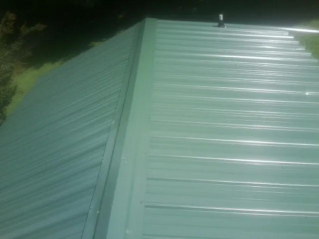New green metal panels meeting at the ridge of a roof — Flat Roof Repair work by our crew in Council Bluffs