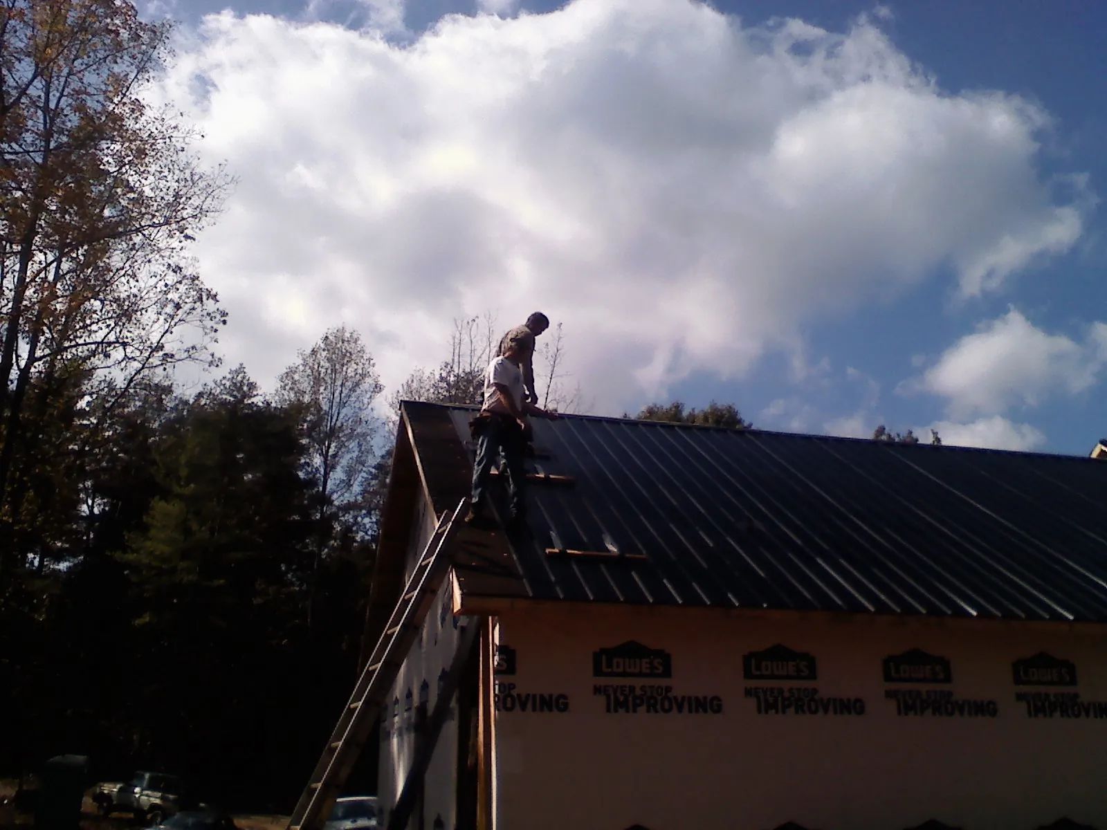 Roofer fastening dark metal panels high against a cloudy sky, from a Roof Inspection job in Council Bluffs