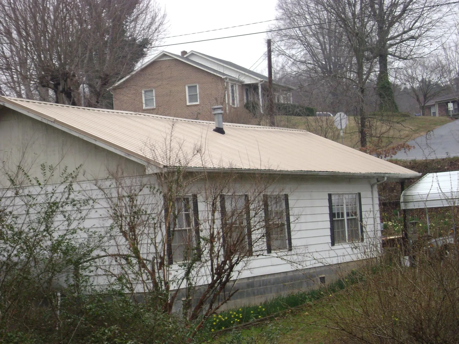 Tan metal roof on a white sided house set into a hillside — Commercial Roofing by Roofing Brothers in Council Bluffs